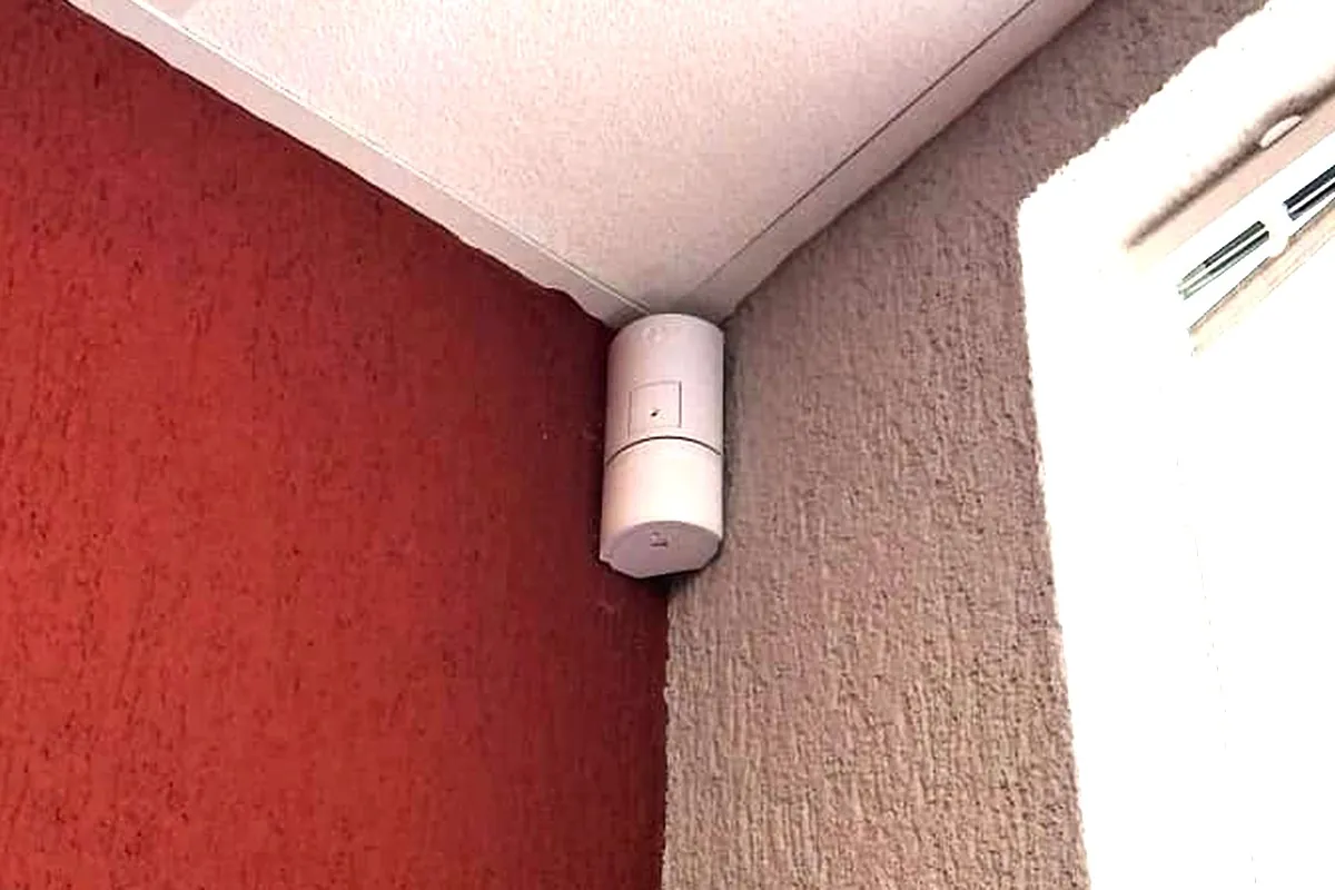 Bílý detektor pohybu v rohu místnosti pod stropním podhledem